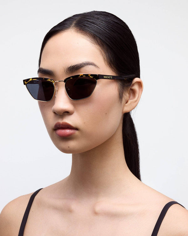 Woman wearing tortoiseshell INDY NEW YORK sunglasses with a plain background